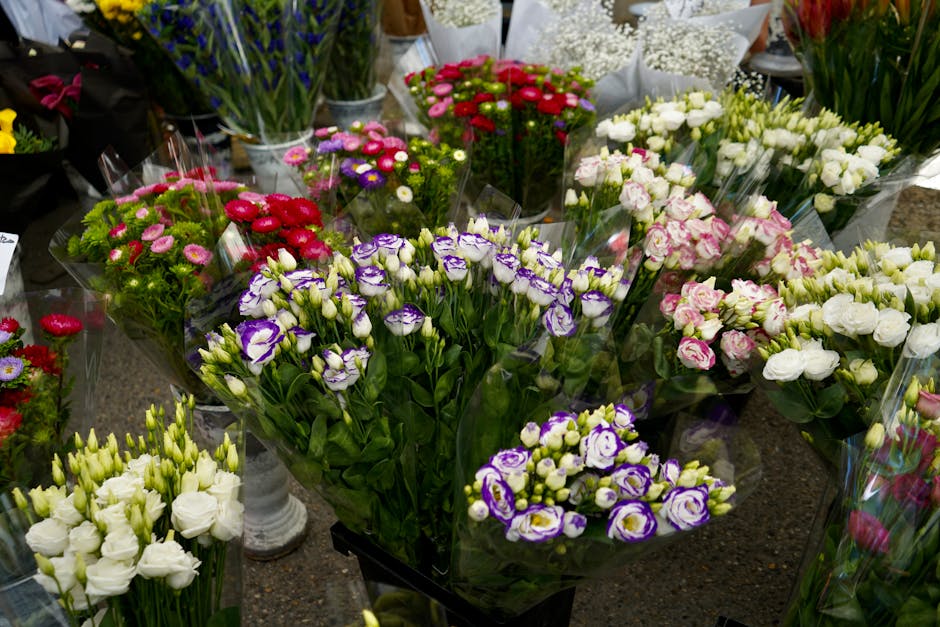 A variety of fresh flowers arranged in bouquets at a florist stall, featuring predominantly white, pink, purple, and red blooms. The arrangement includes lisianthus with delicate white and purple peta